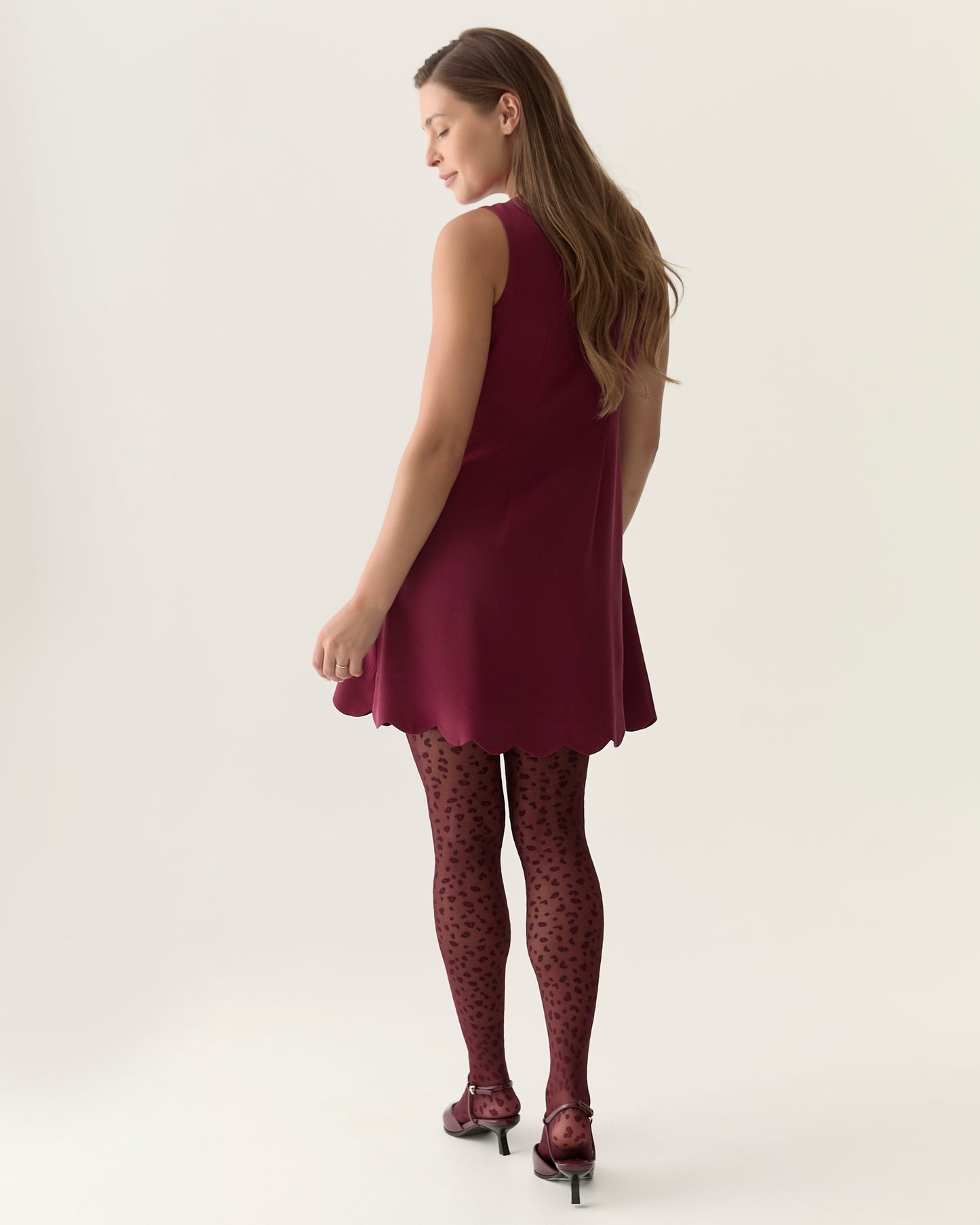 Woman wearing a burgundy dress and patterned tights on a white background