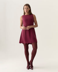 Woman wearing a maroon dress with patterned tights on a white background