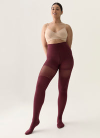 Woman wearing burgundy shaping tights and a beige bra on a white background