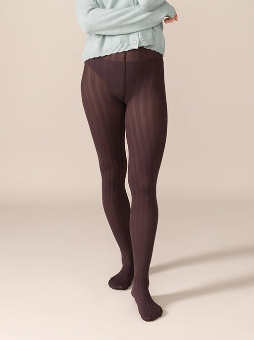 Woman wearing a light blue sweater and dark brown tights against a beige background