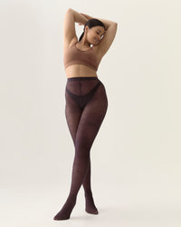 Woman wearing dark brown tights and a beige top on a plain background
