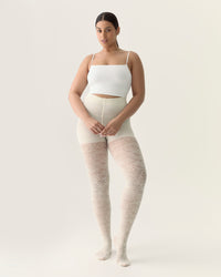 Woman wearing beige tights and a white top on a plain background